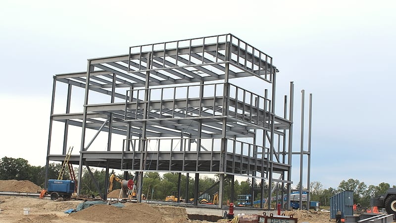 A tower crane above a steel frame at sunrise with construction fencing and stacked materials below.