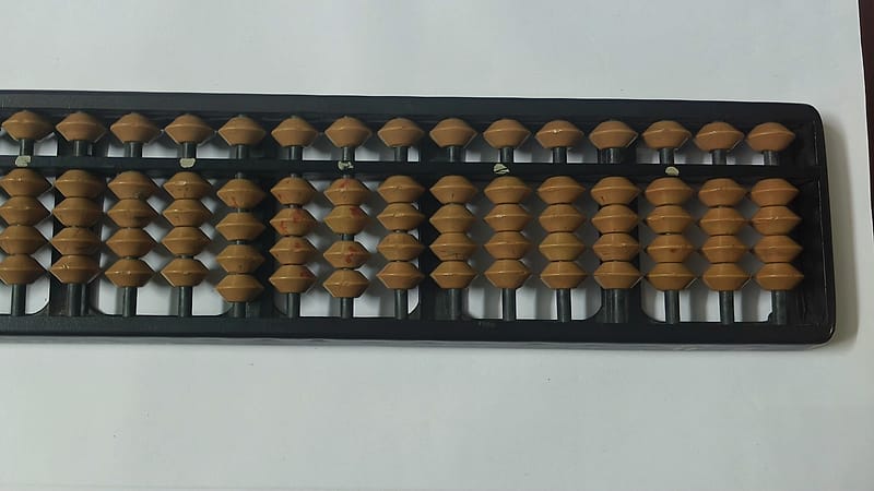 An adding machine with a long paper tape curling onto a desk, printed figures visible along the roll.