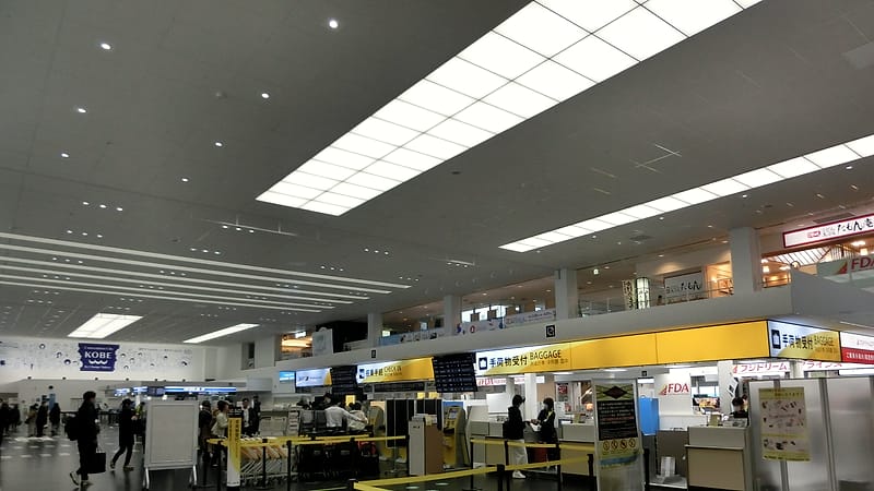 A departure gate with a stroller folded beside a row of chairs, a boarding pass on the seat and planes visible outside.