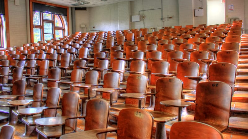 A wooden lectern with a small reading light facing a curved bench of empty high-backed chairs.