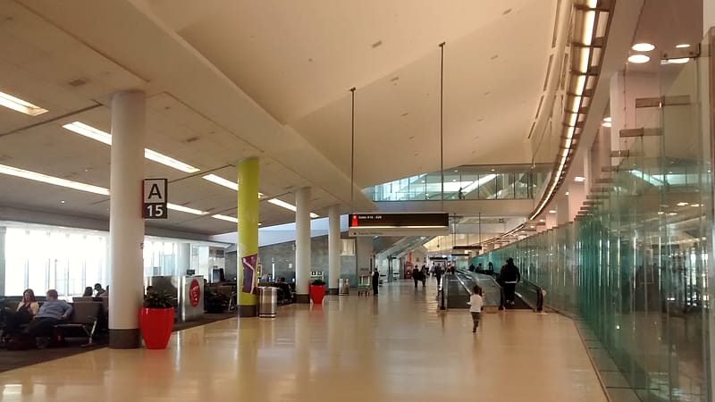 A departures board in an airport terminal with rows of destinations and times above a row of empty seats.