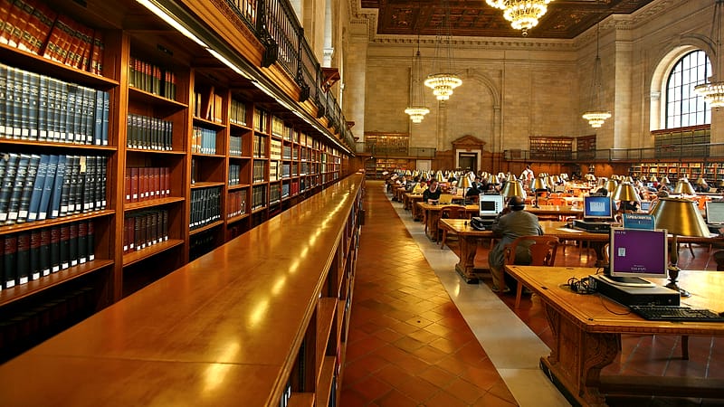 A public reading room with newspapers on wooden rods, a microfilm reader in the corner and long tables under high windows.