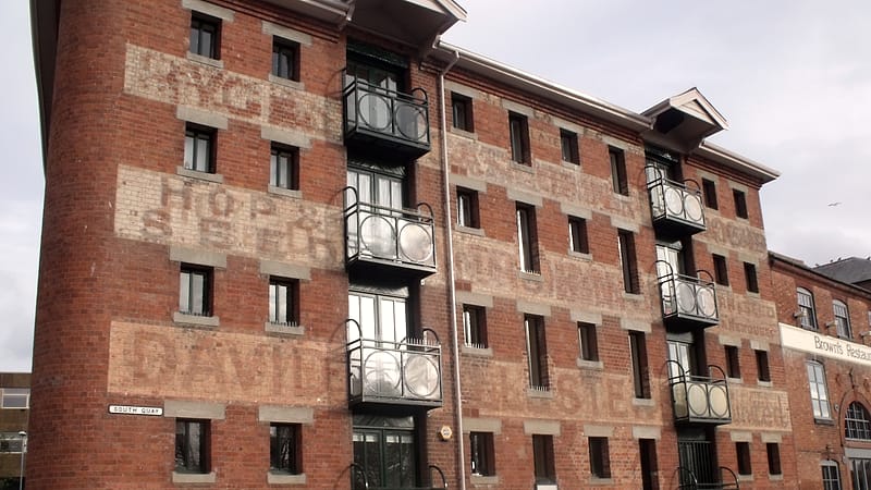 Scaffolding against a masonry mill building with new steel windows installed in the lower openings.