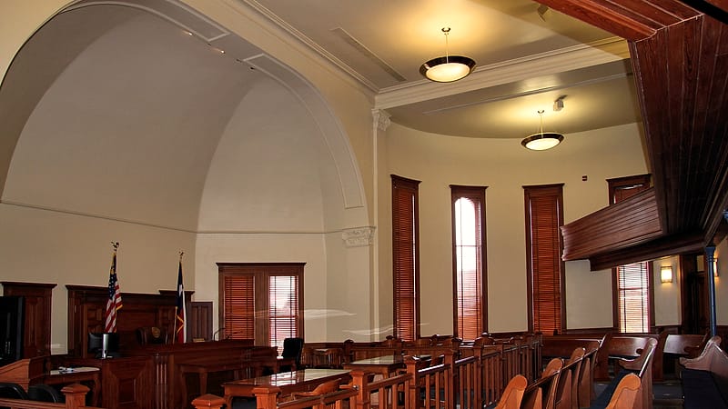 A long empty bench with many identical chairs behind it, seen from the side in a bright room.