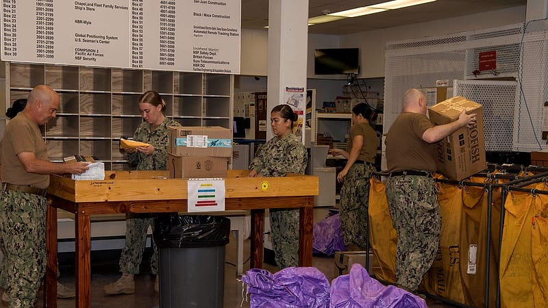 A mail sorting room with canvas trays of envelopes on a metal frame and a clerk's rubber stamp on the bench.