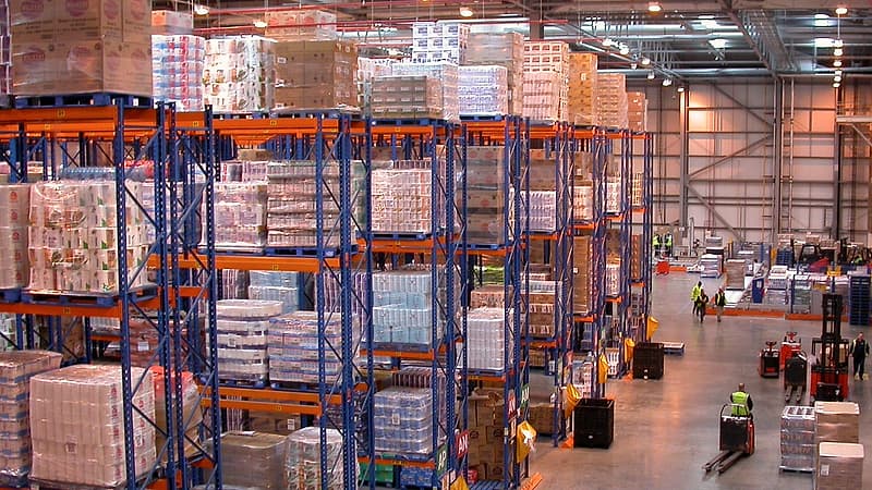 Pallets of cased bottles wrapped in plastic film lined up along a loading dock under fluorescent light.