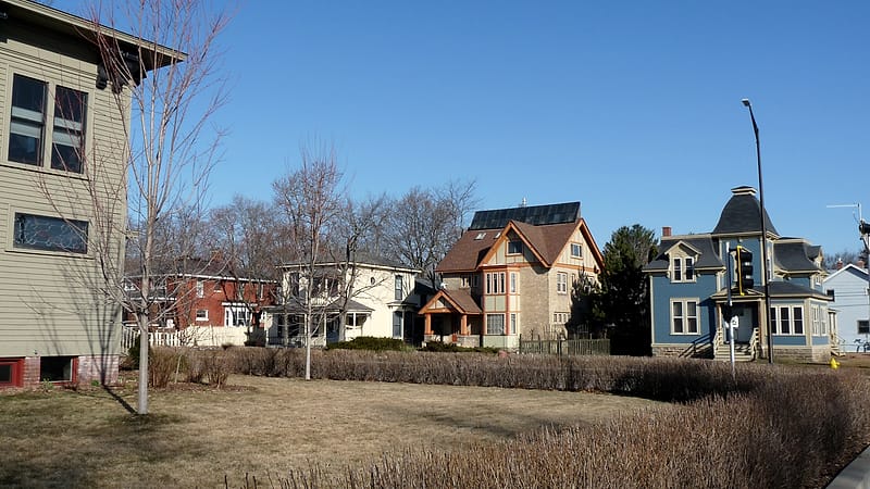 A two-story clapboard house with peeling white paint, a sagging porch roof and an overgrown front yard.